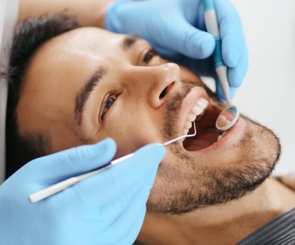 smiling-young-man-sitting-dentist-chair-while-doctor-examining-his-teeth_158595-7733